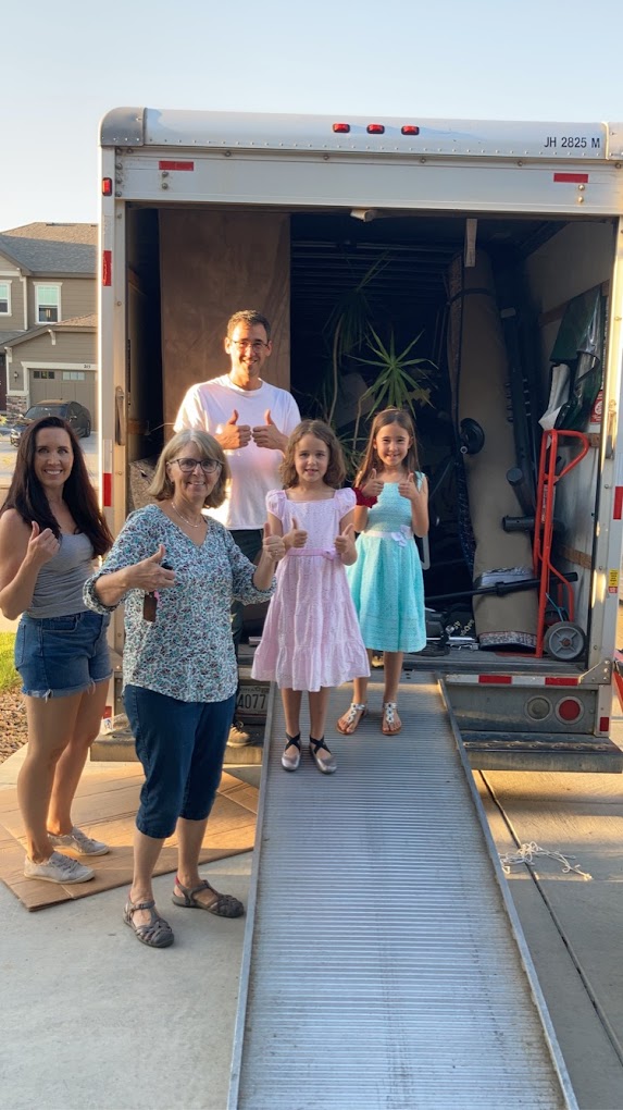 A happy family giving thumbs up at the back of an Anytime Movers truck